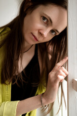 Portrait of middle aged woman with long dark hair standing near window