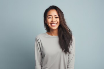 Portrait of a cheerful asian woman in her 20s sporting a long-sleeved thermal undershirt in front of pastel gray background