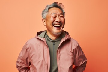 Obraz premium Portrait of a joyful asian man in his 60s wearing a functional windbreaker while standing against pastel brown background