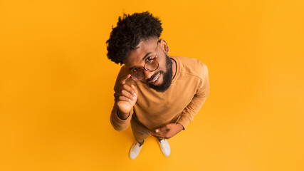 Excited young african man in glasses looking at camera, full body over orange background, top view © Prostock-studio