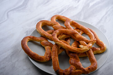 A plate of golden, freshly baked pretzels placed on a sleek white surface. The pretzels have a crispy texture on the outside and are shaped in the traditional knot, perfect for a snack or party