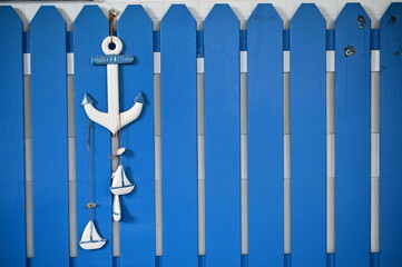 A wooden anchor with small sailboats is seen hanging on a blue outdoor fence, captured during the daytime.