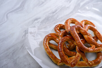 A plate of golden, freshly baked pretzels placed on a sleek white surface. The pretzels have a crispy texture on the outside and are shaped in the traditional knot, perfect for a snack or party