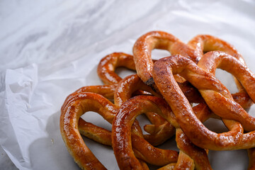 A plate of golden, freshly baked pretzels placed on a sleek white surface. The pretzels have a crispy texture on the outside and are shaped in the traditional knot, perfect for a snack or party