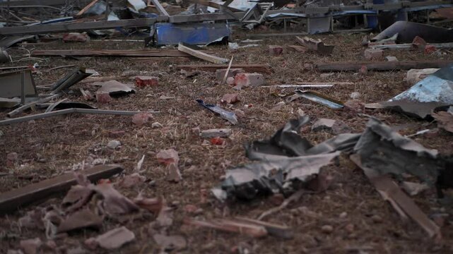 Aftermath of Destruction: Broken bricks, wooden splinters, and mangled metal sheets lie scattered across the barren ground, painting a picture of desolation