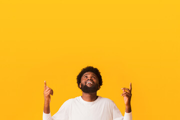 Shocking sale. Positive afro guy looking and pointing up at free space over orange background