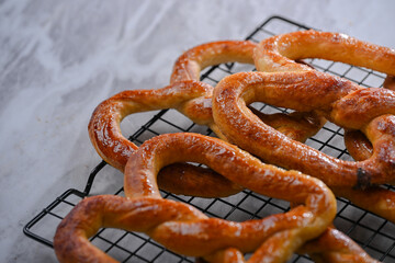 Freshly baked pretzels cooling on a wire rack, their golden-brown crusts glistening. Perfectly shaped and coated with a buttery sheen, these pretzels are a delicious snack ready to be enjoyed