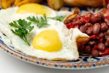 Delicious breakfast plate featuring eggs, beans, bacon, and potato wedges served on a decorative dish