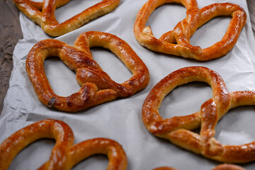 A close-up shot of freshly baked, golden-brown pretzels resting on parchment paper. The pretzels have a glossy, and the wooden background adds a rustic charm to this appetizing scene