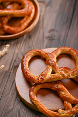 A warm, golden-brown pretzel placed on a round wooden plate, showing its crispy crust and soft texture. The rustic wooden table enhances the simple yet delicious look of this freshly baked treat