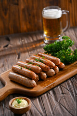 A delicious stack of grilled sausages served on a wooden board, garnished with parsley, and accompanied by a creamy dipping sauce. In the background, a frothy glass of beer