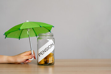 Bank of coins with the inscription Pension and green umbrella. Retirement Insurance concept. Financial support and regular payments to people after retirement. Business and finance