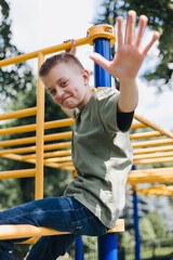 Fototapeta premium A school-age boy in a green T-shirt spends time on horizontal bars, a playground in sunny weather. Front view