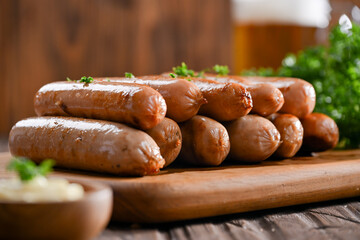 A delicious stack of grilled sausages served on a wooden board, garnished with parsley, and accompanied by a creamy dipping sauce. In the background, a frothy glass of beer