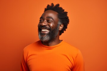 Obraz premium Portrait of a smiling afro-american man in his 50s showing off a lightweight base layer on soft orange background