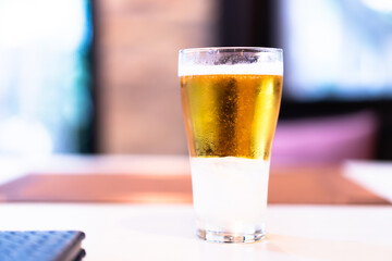 Close-up of cold golden beer in a clear glass on a wooden table, bokeh light background