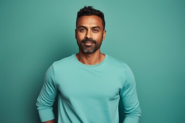 Fototapeta premium Portrait of a satisfied indian man in his 30s sporting a long-sleeved thermal undershirt over soft teal background