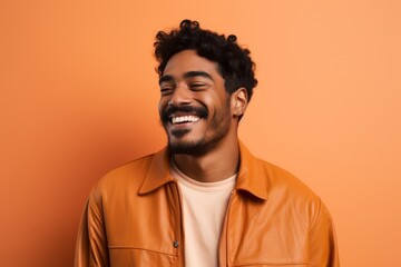 Obraz premium Portrait of a smiling indian man in his 20s wearing a trendy bomber jacket in soft orange background
