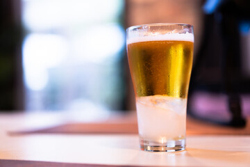 Close-up of cold golden beer in a clear glass on a wooden table, bokeh light background
