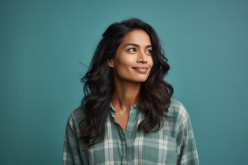 Fototapeta premium Portrait of a glad indian woman in her 20s wearing a comfy flannel shirt isolated in soft teal background