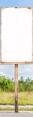 A white sign is standing in a field. The sign is empty and has a wooden post
