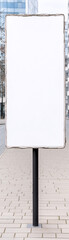 Obraz premium A white sign is standing on a brick sidewalk. The sign is empty and has no writing on it. Concept of emptiness and lack of information