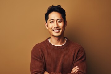 Fototapeta premium Portrait of a content asian man in his 30s wearing a cozy sweater in soft brown background
