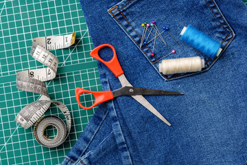 Sewing tools on a cutting mat with denim and thread spools in a craft workspace