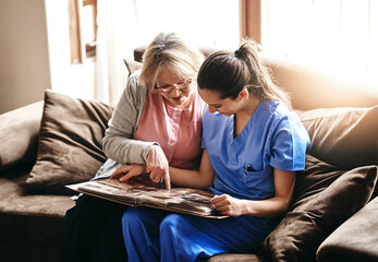 Senior, woman and nurse with photo album in home for memories, nostalgia and remember with support. Elderly, person or female caregiver in assisted living with talking of pictures, patient or bonding