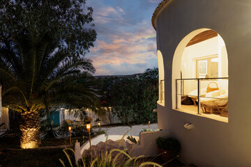 White villa at sunset, late evening, warm window lighting.