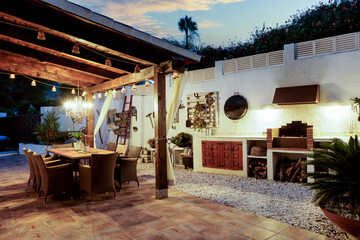 Dining table on the outdoor terrace in the evening. wooden furniture, rustic wall decorations, evening light.