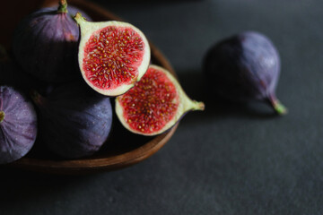 Close up of fresh ripe fig fruits in a wooden bowl on dark grey table 