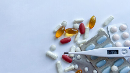 Assortment of multicolored pills, capsules, and a digital thermometer showcasing a normal...