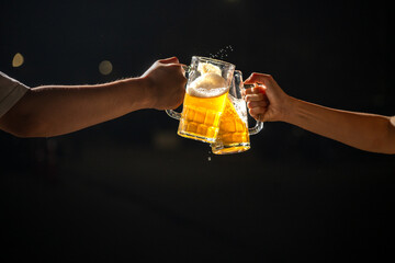 Two hands raise beer mugs overflowing with foam in a lively toast to celebrate Oktoberfest. The...