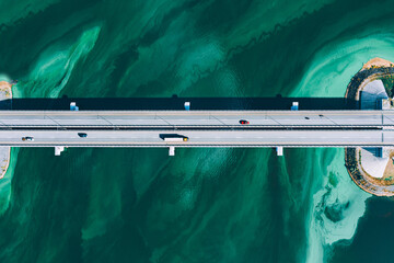 Aerial drone view of asphalt road bridge with cars and truck driving over turquoise blue water...