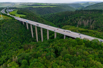 many cargo trucks and cars on the highway on the bridge. asphalt road among green forest and beautiful rain clouds. cargo delivery and transportation concept