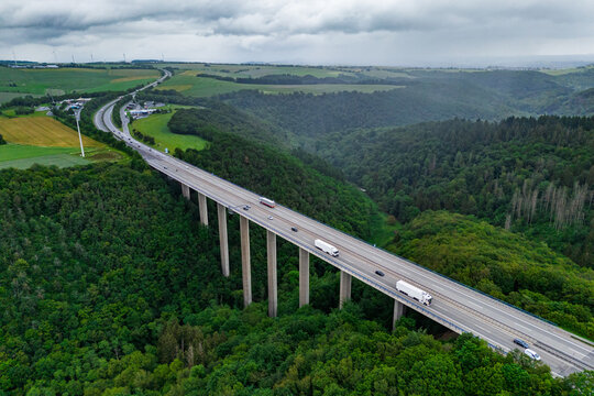 many cargo trucks and cars on the highway on the bridge. asphalt road among green forest and beautiful rain clouds. cargo delivery and transportation concept