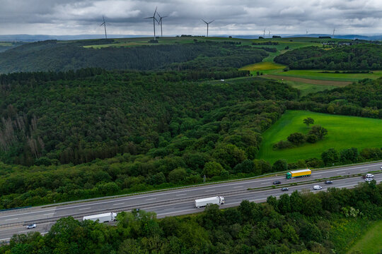 cargo truck and cars on the highway. asphalt road among green forest and beautiful rain clouds. cargo delivery. Wind turbines in the background.