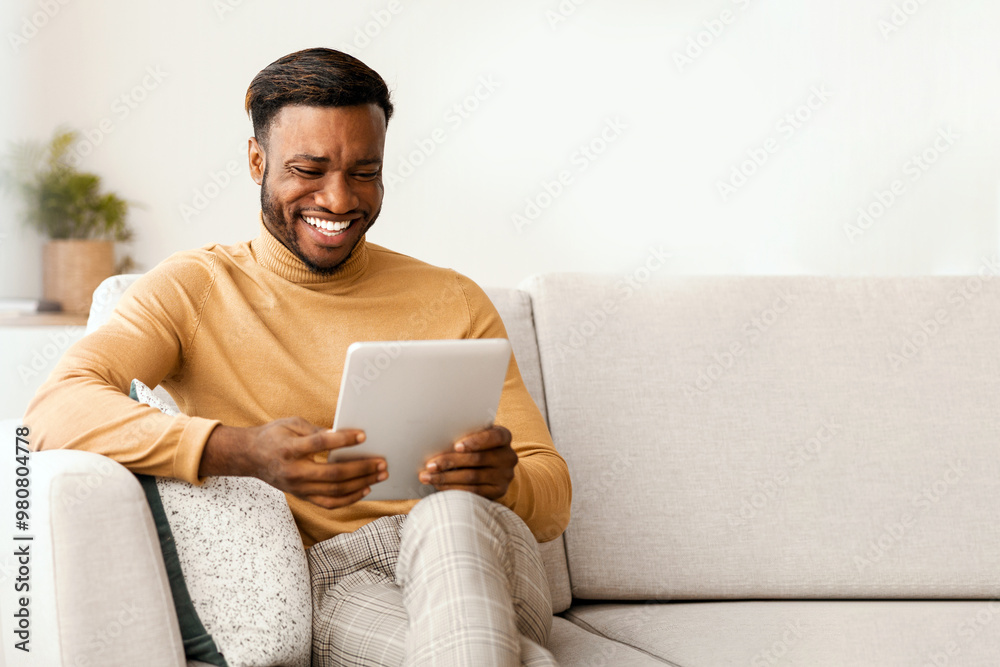 Aufkleber Great App. Smiling Afro Guy Using Tablet Computer Sitting On Couch At Home. Empty Space, Selective Focus