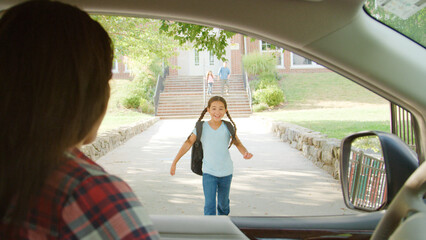 Mother In Car Collecting Daughter In Front Of School Gates