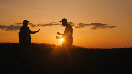 Two farmers dance joyfully in a field, their silhouettes against the sunset sky.
