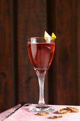 close-up of a Festive red cocktail in a glass with lemon on it. Cooling summer drink on a red background with dried lemons and spoon. Fresh citrus cocktail, healthy drink concept.

