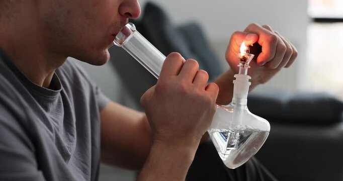 Man lights cannabis with glass water pipe or bong. Legalization and dependence on soft drugs