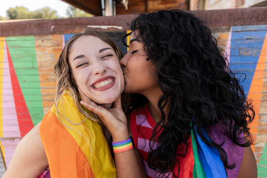Multiracial lesbian couple kissing in park, wrapped in pride flag