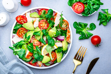 Fresh salad with avocado, chicken, tomatoes and lettuce, gray background, top view