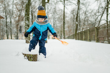 Adorable little boy having fun on snowy winter day. Cute child wearing warm clothes playing in a snow.