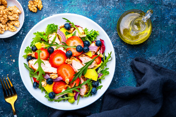 Foodie food salad with strawberry, chicken, arugula, blueberries, avocado and walnuts, blue table., top view