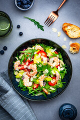 Foodie food salad with shrimp, strawberries, onion, arugula and almond petals, gray background, top