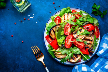 Vegan salad with grilled vegetables, tomatoes and mixed herbs. Blue background, top view