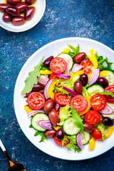 Vegan salad with olives, tomatoes, paprika, cucumber, lettuce and onion. Blue background, top view